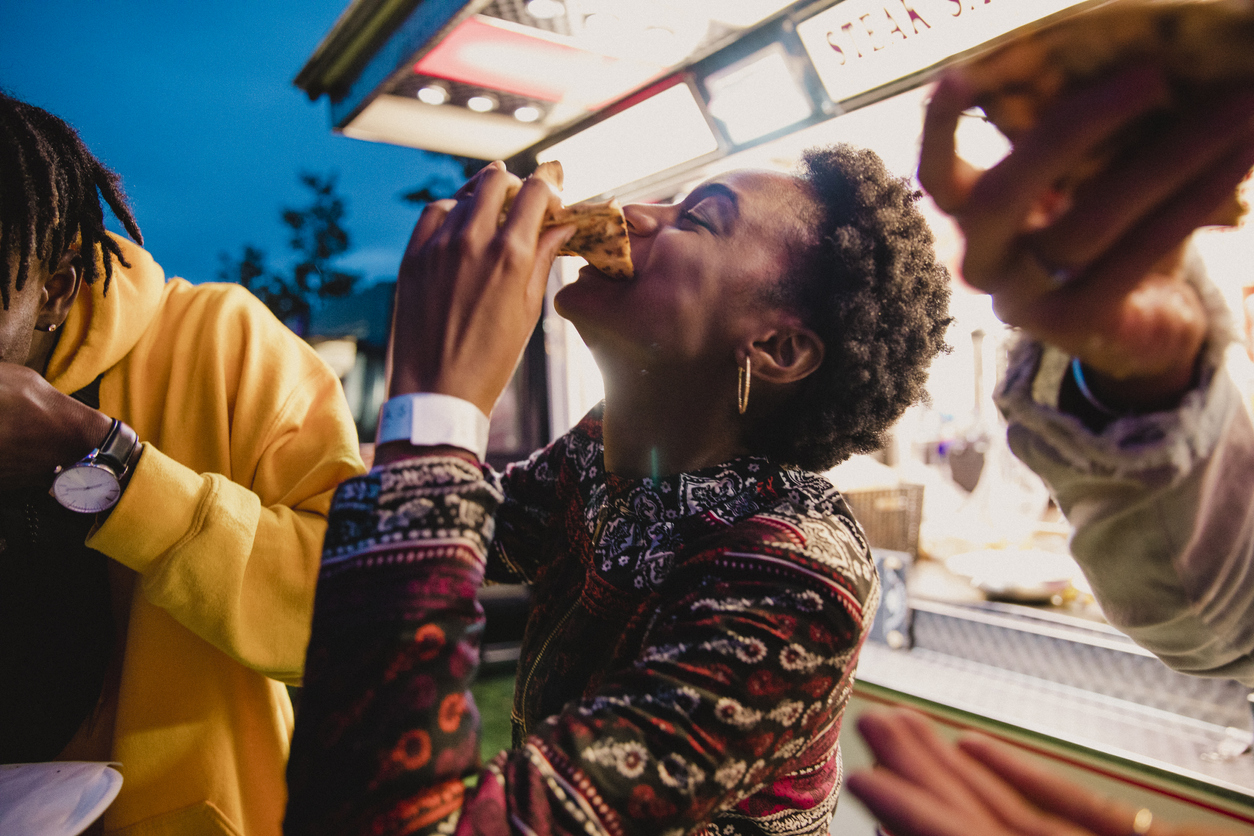 Young woman eating pizza, laughing and enjoying time with her friends.